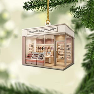 May include: A rectangular hanging ornament shaped like a storefront with the text WILLIAMS BEAUTY SUPPLY on the facade. The interior displays shelves of cosmetics, hair care products, and mannequin heads with wigs, all rendered in soft pink and wood tones.