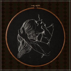 May include: A circular wooden embroidery hoop containing black fabric with a white cross-stitch design. The embroidery depicts a side profile of a person with long hair, with one hand raised to their head and the other near their face.