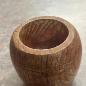 Peut inclure: Une petite tasse en bois en forme de tonneau avec une finition marron naturel et des motifs de grain de bois visibles. Le récipient présente un corps arrondi, une large ouverture circulaire au sommet et des lignes gravées horizontalement.