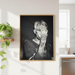 May include: A black and white portrait print in a gold frame featuring a person with extensive arm and neck tattoos, covering their face with one hand. The person wears a dark shirt and has a rose tattoo visible on the back of their hand.