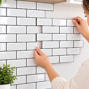 May include: A set of white rectangular subway tile stickers with black grout lines. The adhesive tiles are arranged in a staggered brick pattern, featuring a glossy finish that mimics the appearance of traditional ceramic wall tiles.