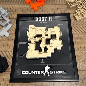 May include: A framed 3D wall art piece featuring the Dust II map from Counter-Strike. The beige map layout is mounted on a black background with white text labels including Bomb Site A, Bomb Site B, CT Spawn, T Spawn, T Ramp, and Upper Tunnels.