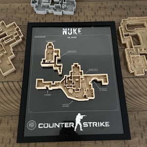 May include: A framed 3D map of the Nuke level from Counter-Strike, featuring a tan plastic layout on a dark background with labels for Bomb Site A, Bomb Site B, T Spawn, CT Spawn, and Outside. Two additional unmounted map pieces are visible nearby.