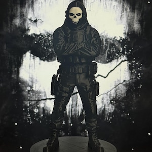 May include: A black figurine of a soldier wearing a skull mask and tactical gear, standing with arms crossed. The figure is mounted on a circular base featuring the text CALL OF DUTY GHOST in white lettering against a dark, textured background.