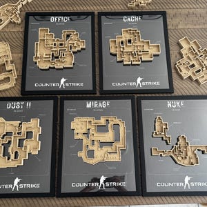 May include: Five framed wall art pieces featuring 3D wooden maps of Counter-Strike game levels including Office, Cache, Dust II, Mirage, and Nuke. Each black frame contains a gray background with the map name, game logo, and a raised wooden layout.