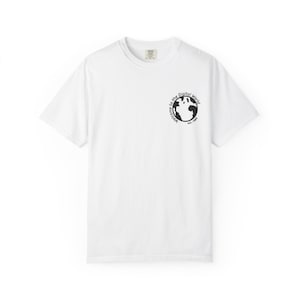 May include: A white short-sleeve t-shirt featuring a small black circular graphic on the upper left chest. The graphic depicts a stylized globe silhouette surrounded by the text Welcome to the Digital World est. 1985 in a circular black font.