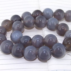 May include: A strand of grey agate beads, each bead is round and smooth. The beads are strung on a clear thread.
