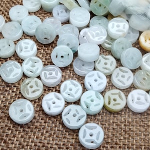 May include: A collection of round, white jade beads with a carved design. The beads have a hole in the center and are strung together on a string.