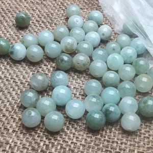 May include: A collection of round, light green jade beads. The beads are smooth and polished, and they have a translucent appearance.