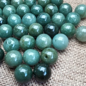 May include: A collection of smooth, round, green jade beads. The beads are arranged in a random pattern on a brown burlap surface.