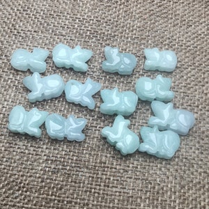 May include: A collection of 15 jade green carved animal charms. The charms are in the shape of various animals, including butterflies, fish, and other creatures. The charms are all made of a light green jade stone.
