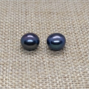 May include: Two dark blue round pearls on a beige fabric background.