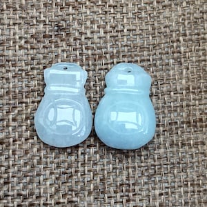 May include: Two light blue jade pendants shaped like Chinese money bags. The pendants have a smooth, polished finish and are carved with intricate designs.