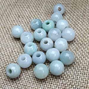 May include: A collection of 18 light green jade beads, each with a hole in the center. The beads are arranged in a loose pile on a brown burlap surface.