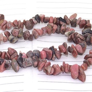 Puede incluir: Una hebra de cuentas de piedras preciosas rosadas y grises. Las cuentas tienen una forma irregular y un acabado natural y pulido.