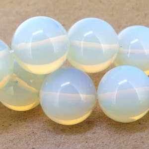 May include: A close-up of a string of opalescent, round beads. The beads are a soft white colour with a subtle, pearly sheen. The beads are strung together, creating a continuous line of spherical shapes. The background is a light brown.
