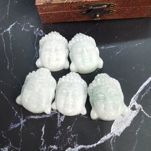 May include: Five jade green Buddha head pendants, each with a serene expression and intricate details. The pendants are carved from a smooth, polished jade stone.