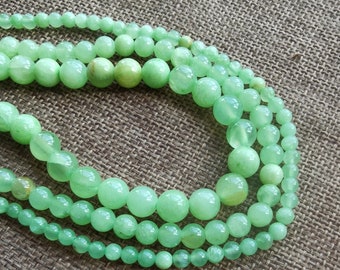 May include: Three strands of light green jade beads, each strand with a different size of beads. The beads are round and smooth.