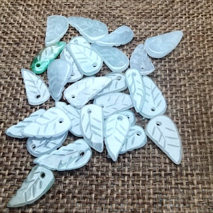May include: A collection of white leaf-shaped pendants with a green leaf pendant in the center. The pendants are made of a translucent material and have a smooth, polished finish.