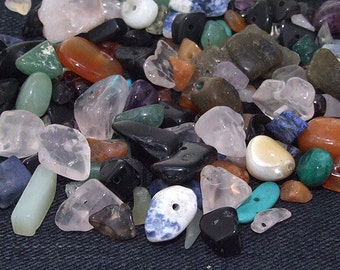 May include: A collection of various tumbled stones in different colours and shapes, including rose quartz, amethyst, black obsidian, and turquoise. The stones are arranged on a dark blue fabric background.