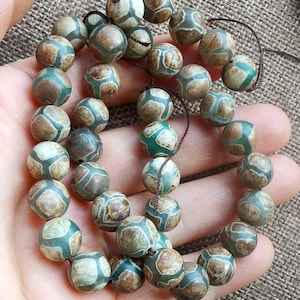 May include: A string of green and brown agate beads. The beads are round and have a mottled pattern. The string is made of brown cord.