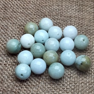 May include: A collection of round, polished beads in shades of green and white. Each bead has a small hole, suggesting they are for stringing. The beads vary in color, from pale green to a creamy white, with a glossy finish.