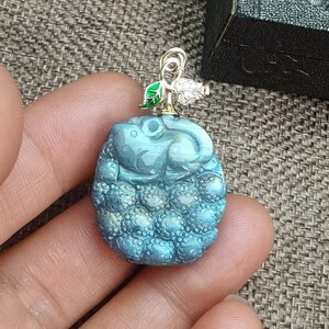 Puede incluir: Un colgante de labradorita azul con un diseño de ratón tallado, una hoja verde y un pequeño acento de diamante. El colgante está en una cadena de oro.