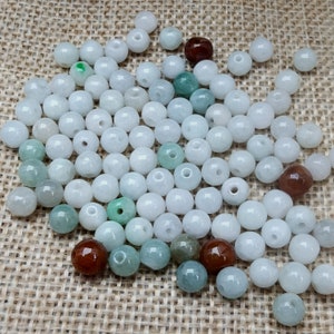 May include: A large collection of white, green, and brown jade beads. The beads are round and smooth, and they are arranged in a random pattern.