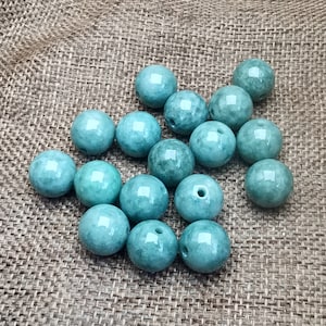 May include: A collection of 15 smooth, round, teal green jade beads. The beads are arranged in a cluster on a brown burlap surface.