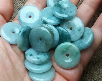 Può includere: Una collezione di perline di giada verde a forma di ciambella con un foro al centro. Le perline sono lisce e lucidate, e hanno un colore verde chiaro.