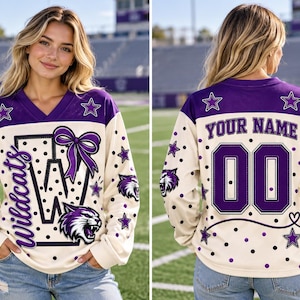 May include: A long-sleeve V-neck jersey in cream with purple accents, featuring a large letter W, a purple bow, and a wildcat mascot graphic on the front. The back displays the text YOUR NAME above the number 00, surrounded by purple star patterns.