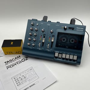 May include: A blue Tascam Ministudio Porta02 cassette recorder with multiple control knobs, two vertical faders, and a cassette deck. Included are a yellow and black Triad box and a white paper owner's manual with a line drawing of the device.