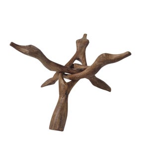 May include: A brown wooden display stand crafted from three interlocking pieces of carved wood. The stand features a tripod base with three upward-curving arms that meet in the center to form a stable support structure with a natural wood grain.