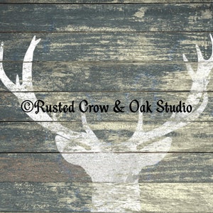 Pu&ograve; includere: Una silhouette bianca di una testa di cervo con corna su uno sfondo di legno blu e grigio invecchiato. Il testo "Rusted Crow & Oak Studio" &egrave; stampato sotto la testa di cervo.