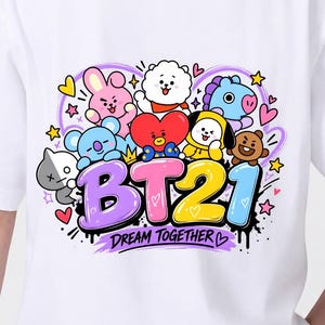 May include: A white t-shirt featuring a colorful graphic print of BT21 characters including a red heart, pink rabbit, white sheep, blue horse, yellow dog, and brown bear. The text BT21 and DREAM TOGETHER are printed in bold, stylized lettering.