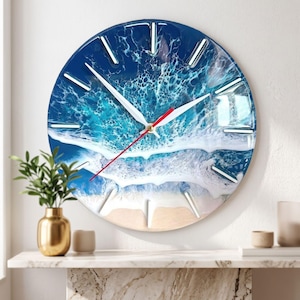 May include: A round wall clock featuring a resin art design of ocean waves crashing onto a sandy beach. The clock face displays a deep blue sea, white foam, and a beige shoreline. It has white hour markers and white clock hands with a red second hand.