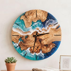May include: A round wall clock featuring a natural wood grain center combined with blue and turquoise resin accents that mimic ocean waves with white foam details. The clock has simple black hour markers and black hands.