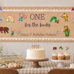 May include: A rectangular tan birthday banner featuring colorful illustrations of storybook characters, with the text ONE for the books and Happy 1st Birthday Hudson! The banner has a scalloped white border and small triangular flags at the corners.