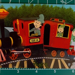 Puede incluir: Una ilustración de postal de estilo vintage de una locomotora de vapor roja etiquetada como OLDE 101, con tres personajes de dibujos animados con sombreros puntiagudos en los vagones. El tren está sobre un puente de caballetes ante un bosque.