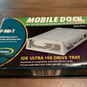May include: A rectangular cardboard box for an inClose Mobile Dock P-96i-T IDE Ultra 100 drive tray. The packaging is green, black, and blue with white text, featuring an image of a light gray plastic drive tray chassis and a barcode.