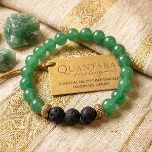 Puede incluir: Una pulsera de cuentas con cuentas de aventurina verde lisa, tres cuentas de lava negra porosas y dos cuentas espaciadoras doradas texturizadas. Una etiqueta rectangular de color canela lleva impreso el texto: QUANTARA Healing ESSENTIAL OIL DIFFUSER BRACELET HANDMADE LUXURY.
