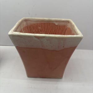 May include: A square ceramic planter with a tapered base, featuring a matte terracotta-colored exterior and a contrasting thick, textured white glaze dripping over the top rim, creating a distinct two-tone appearance on the vessel.