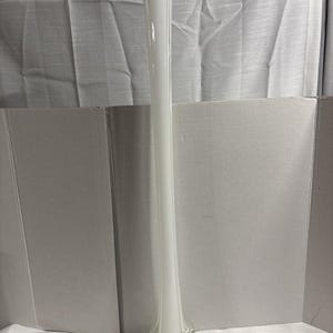 May include: A tall, slender, white glass bud vase with a smooth, elongated neck that flares slightly at the top. The base of the vase features a clear, multi-pointed glass design that provides stability and a decorative element to the structure.