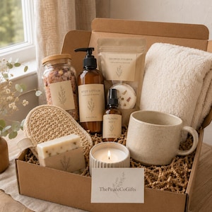 May include: A gift box containing a glass jar of bath salts, a brown pump bottle of body lotion, a shower steamer pouch, a beige towel, a textured loofah, a bar of soap, a calming mist spray, a lit candle, a speckled mug, and a card labelled ThePeaceCoGifts.