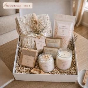Puede incluir: Una caja de regalo etiquetada Natural Retreat - Box 1 que contiene una manta beige de espiga, una bolsa de sales de baño rosas, dos paquetes de té, una pastilla de jabón, un tarro de exfoliante de avena, una vela de soja y una cuchara de madera.