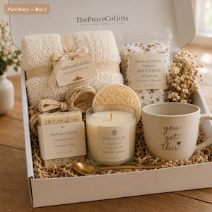 Puede incluir: Una caja de regalo que contiene una manta texturizada de color crema con etiqueta, una bolsa de sales de baño, una esponja vegetal redonda, una pastilla de jabón de avena y karité, una vela de soja de vainilla y cachemira, una cuchara dorada y una taza con el texto you got this.