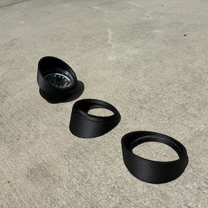 May include: Three black, circular gauge pods with a textured finish. One pod contains a round analogue gauge with a white face, black markings, and a needle. The other two pods are empty, featuring a slanted, cylindrical design for housing instruments.