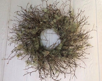 May include: A circular wreath constructed from thin, dark brown natural twigs and branches. The structure is densely interwoven and accented with patches of light, pale green lichen or moss distributed throughout the woody frame.