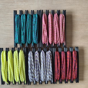 May include: A collection of twelve bundles of twisted cord, each wrapped around a black plastic bobbin. The cords feature various colors including teal, pink, neon yellow, white with purple flecks, and red with orange flecks, arranged in two rows.