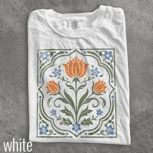 May include: A white t-shirt featuring a central graphic print of three orange tulips with green stems and leaves, surrounded by small blue flowers and a decorative green border. The inner neck label displays the text Comfort Colors.